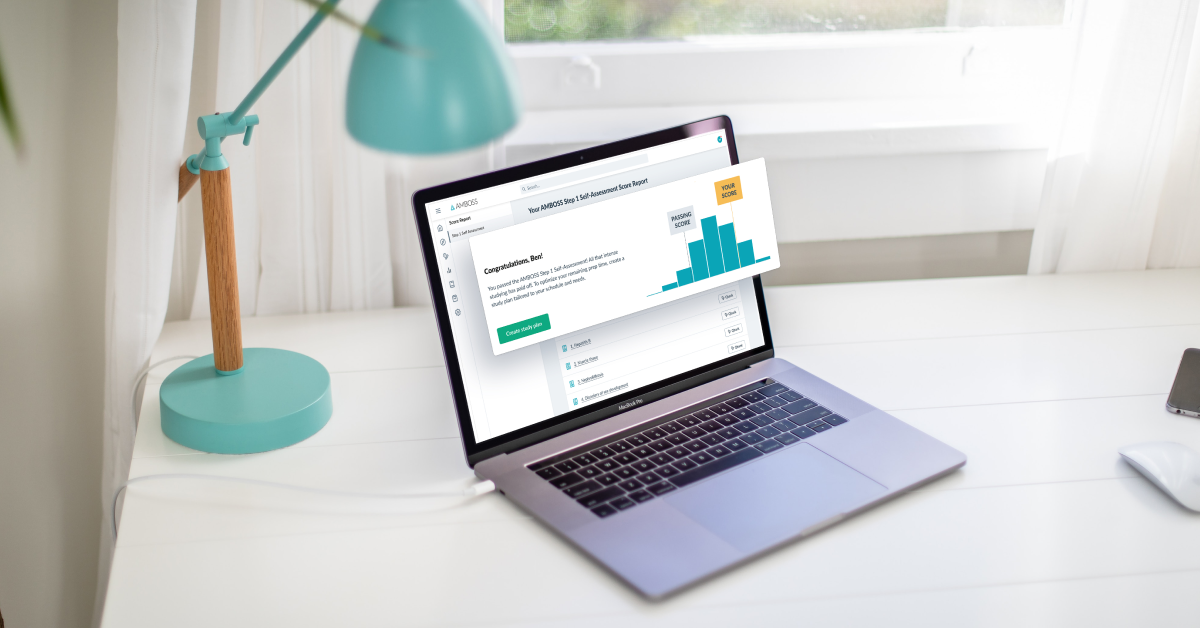 A laptop screen shows the score report from the AMBOSS Step 1 Self-Assessment.