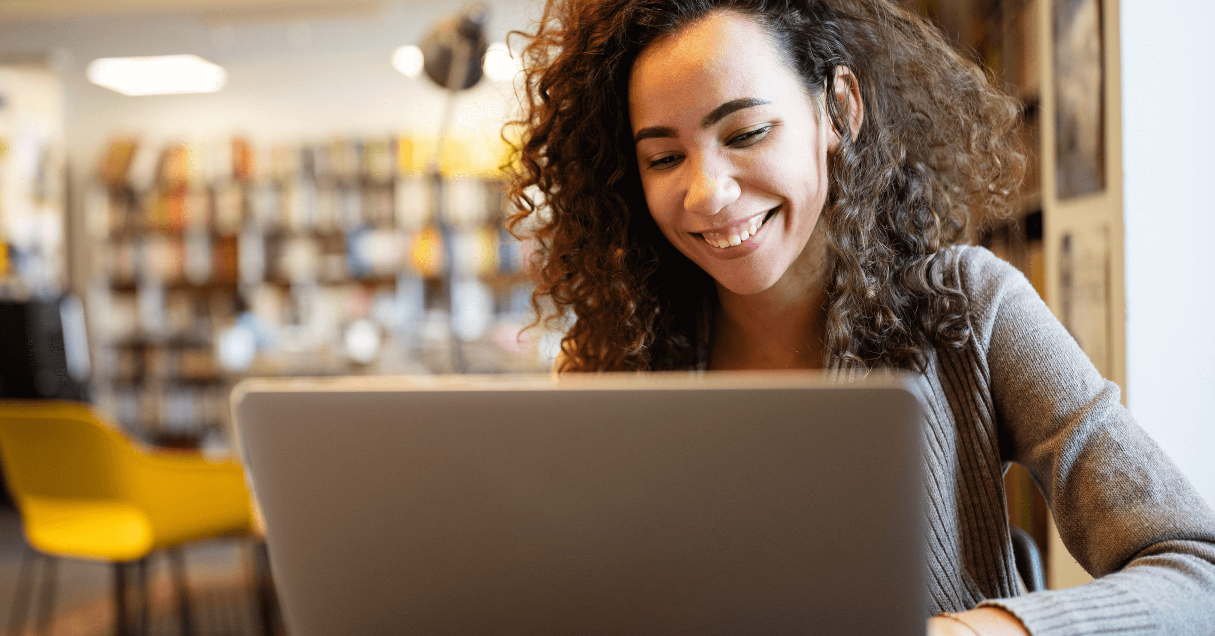 A young woman smiles while looking at her laptop computer. 