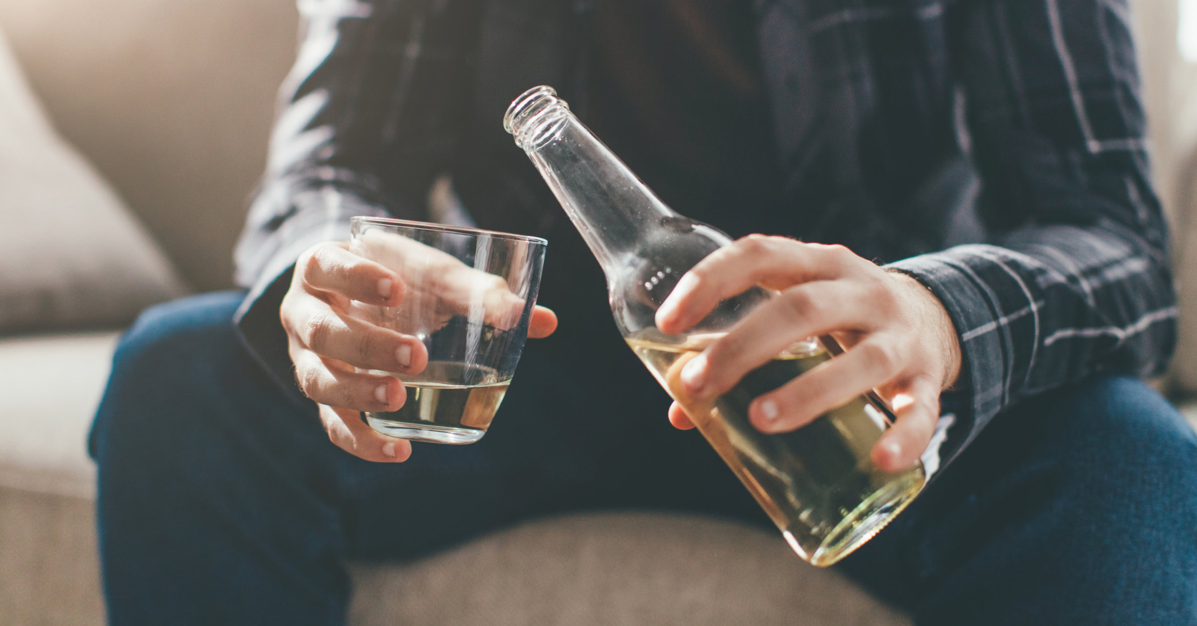 Ein Mensch sitzt auf dem Sofa und schenkt ein Getränk von der Flasche in ein Glas.