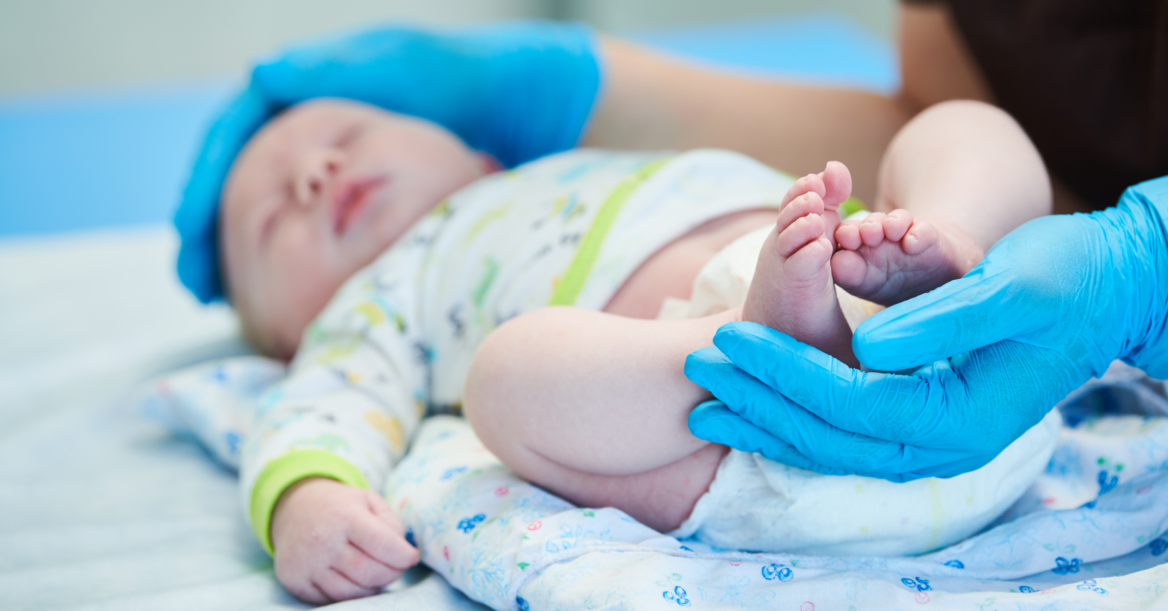 Ein Säugling wird von einer Person mit blauen Untersuchungshandschuhen untersucht. SIDS und BRUE im AMBOSS-Blog.