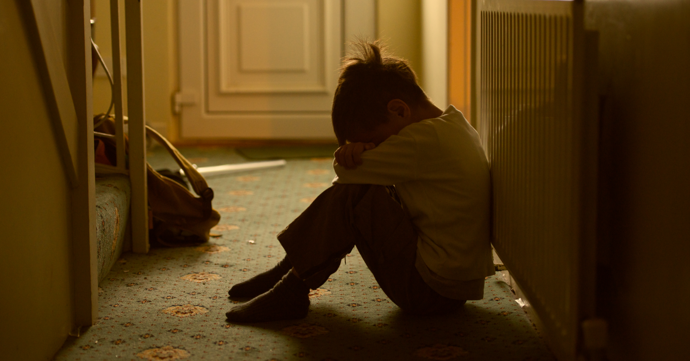 Ein Kind sitzt mit angezogenen Knien auf dem Fußboden und versteckt sein Gesicht. Medizinischer Kinderschutz im AMBOSS-Blog.